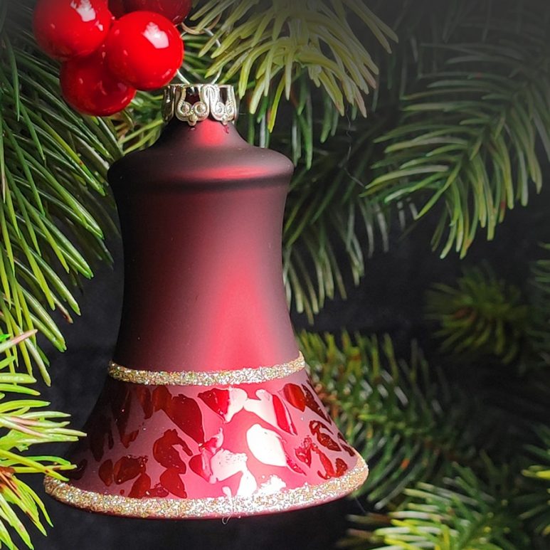Christbaumglocke aus Glas in einem dunklen Rotton und Softeffekt hängend in einem Zweig mit Beeren