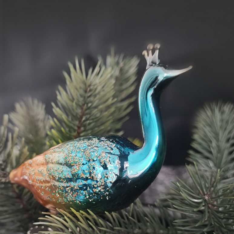 Nahaufnahme vom Pfau aus Glas in grünen Zweigen