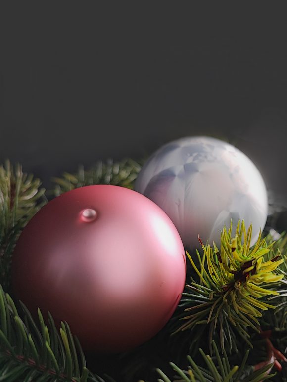 2 Christbaumkugeln aus Glas liegen dekorativ auf Tannenzweige - eine Kugeln in Rosé matt und eine in weiß Icing Design